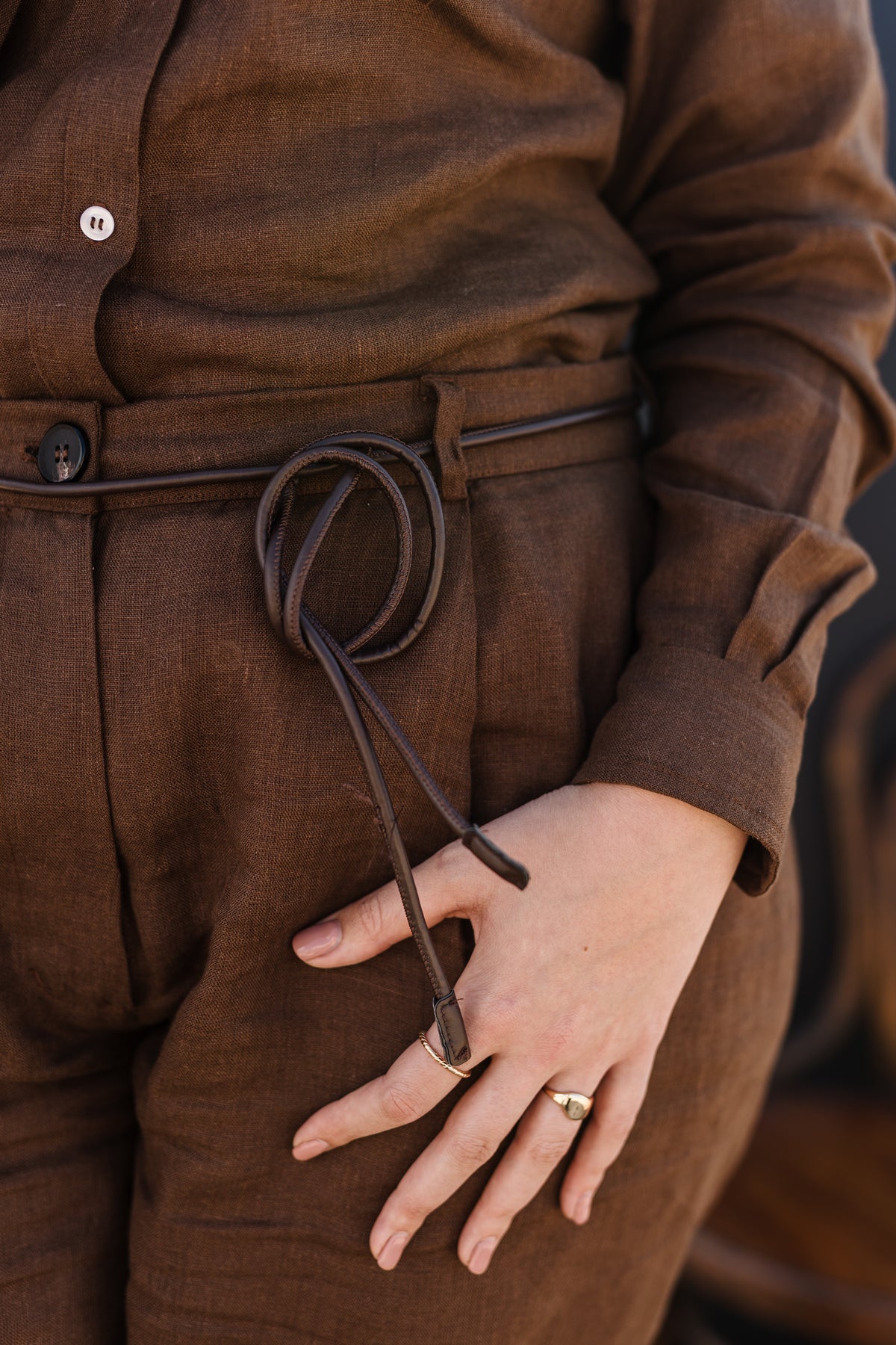 A close-up of a person wearing a matching Lowveld Umber 100% European brown linen button-up shirt and  Lowveld Umber 100% European brown linen pants
